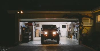 A Jeep wrangler sitting in an open garage at night with the headlights on.
