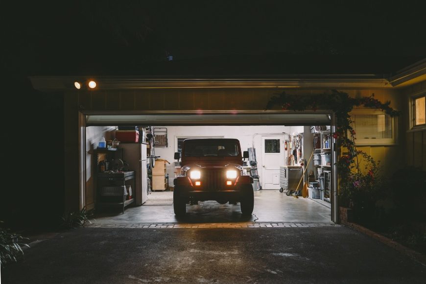 A Jeep wrangler sitting in an open garage at night with the headlights on.