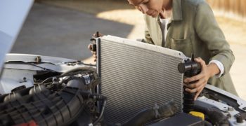A woman showing how to install a radiator by sliding it into the front part of her car.