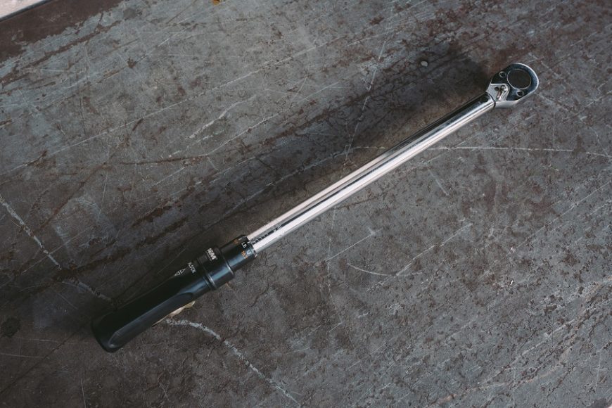 A torque wrench sitting on top of scratched concrete flooring.