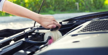 A woman tightening the lid on her vehicle's antifreeze reservoir.