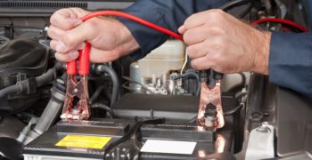 Man showing how to connect jumper cables to the the posts of a car battery.
