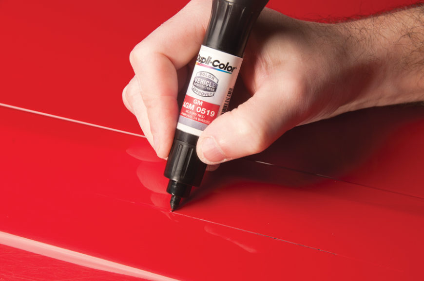 person demonstrating how to use car paint touch up on a red vehicle.