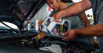 A daughter watches as a her father pours STP synthetic motor oil to show her how to change the car's oil.